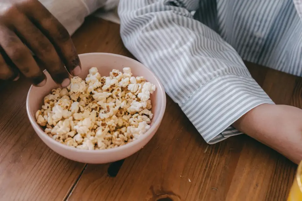 A bowl of plain popcorn sitting next to a dog resting on a couch
