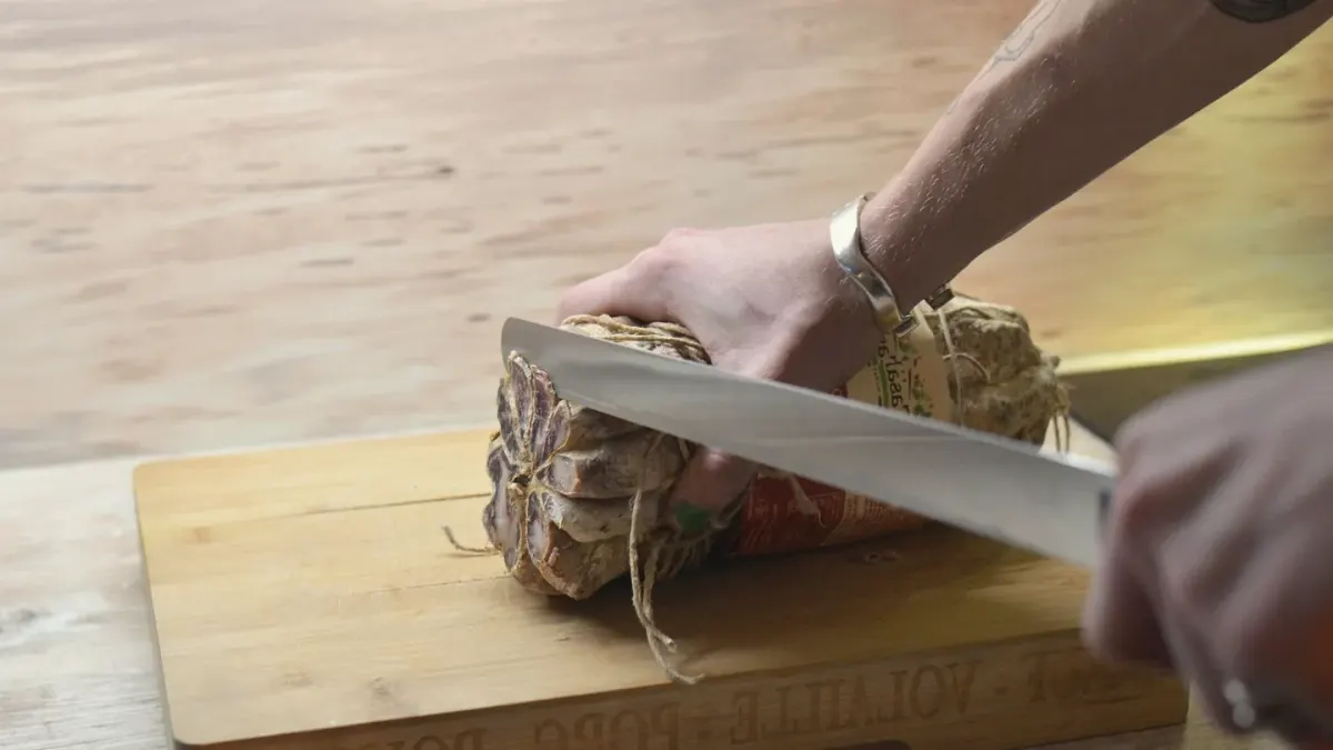 A cutting board of sliced ham with a dog sitting nearby and watching