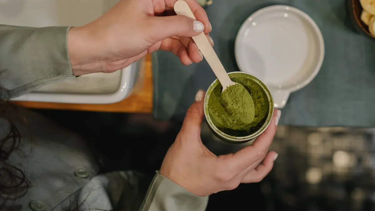 A dog owner scooping a powdered supplement over kibble in a stainless steel bowl