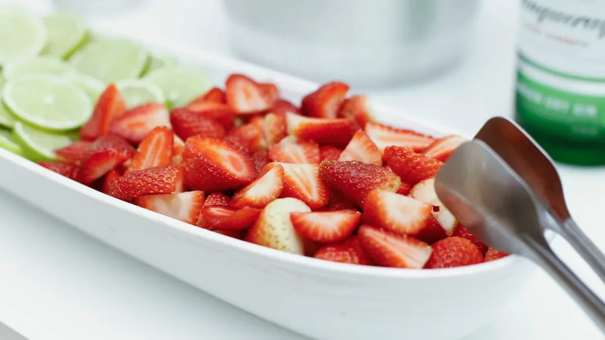 Sliced strawberries in a stainless steel bowl next to a resting athletic dog on turf